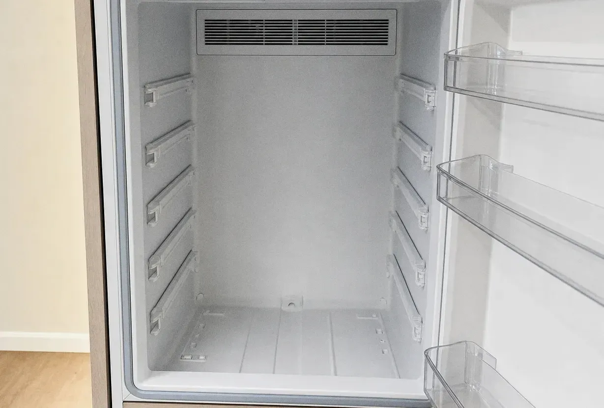 Empty white refrigerator interior with glass shelves and open door bins