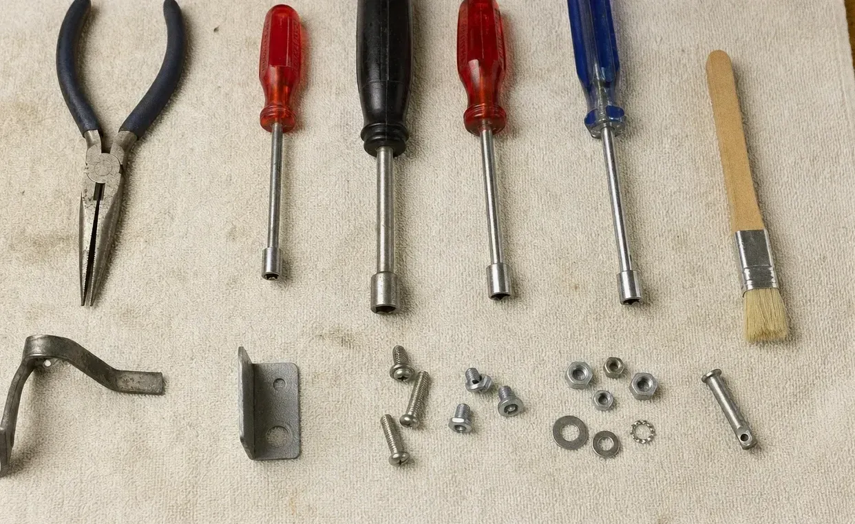 Pliers, coloured screwdrivers, a long brush, a hinge bracket and loose screws and washers on a canvas cloth